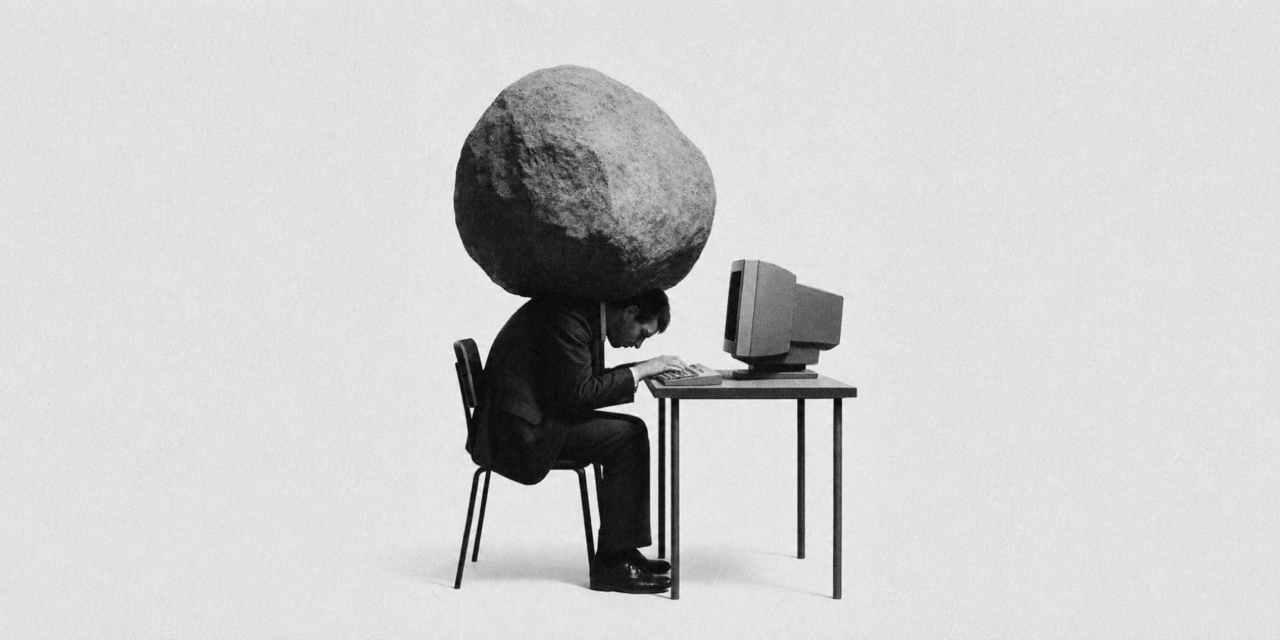Schwarz-Weiß-Foto: ein Mann am alten Computer mit einem riesigen Felsen als Kopf, Sinnbild für die Last der Technik
